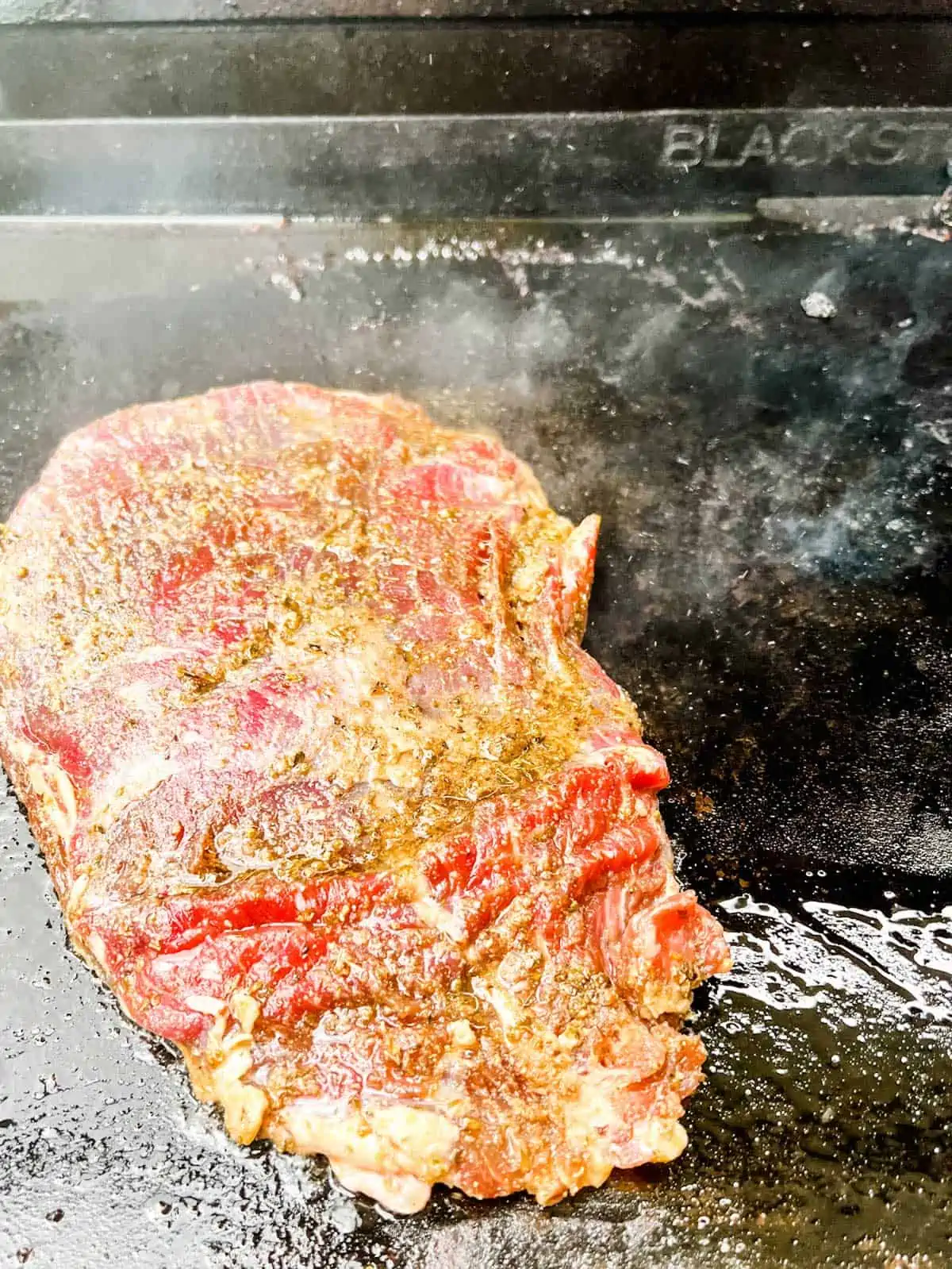 Photo of flank steak cooking on a blackstone griddle.
