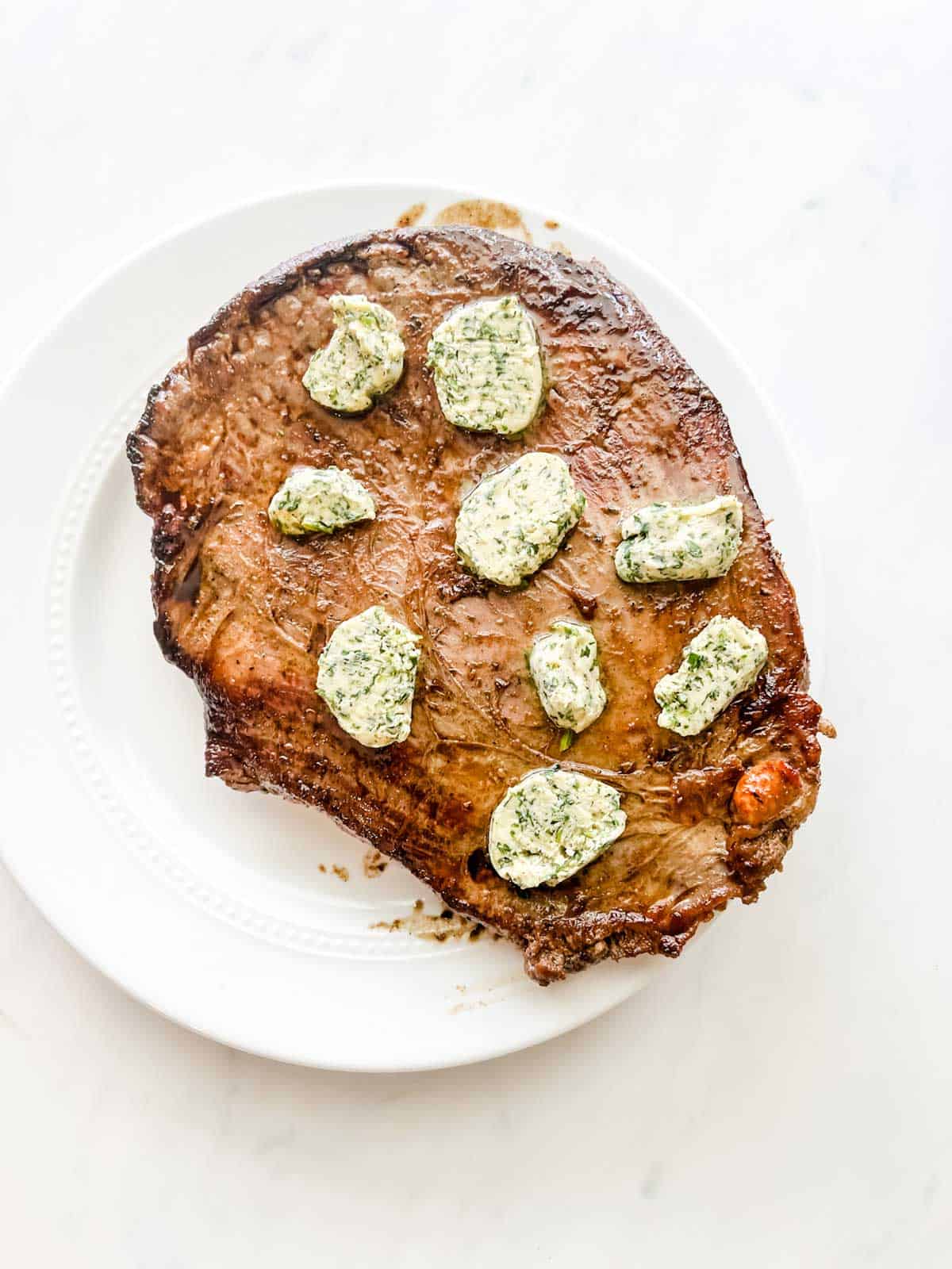 Photo of flank steak resting with herb butter on top.