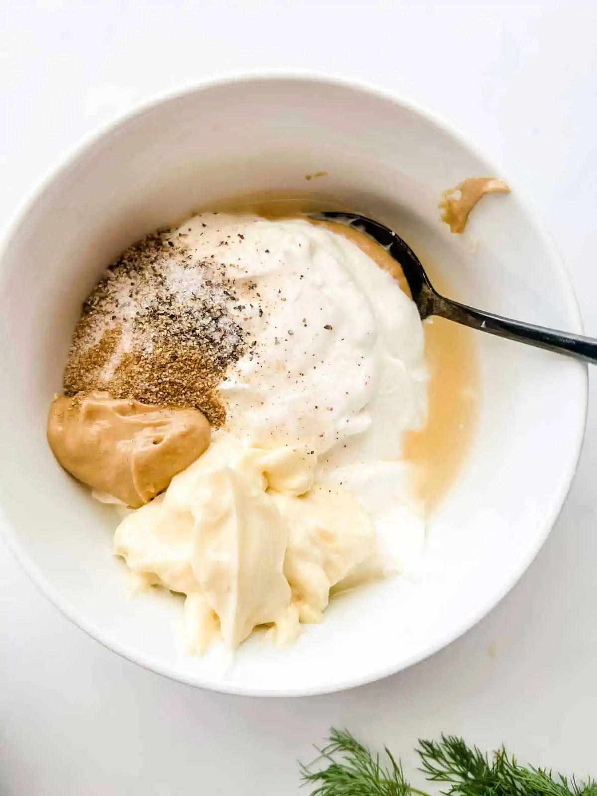 Overhead photo of sour cream, mayo, dijon mustard, apple cider vinegar, celery salt, sea salt, and black pepper in a small bowl.