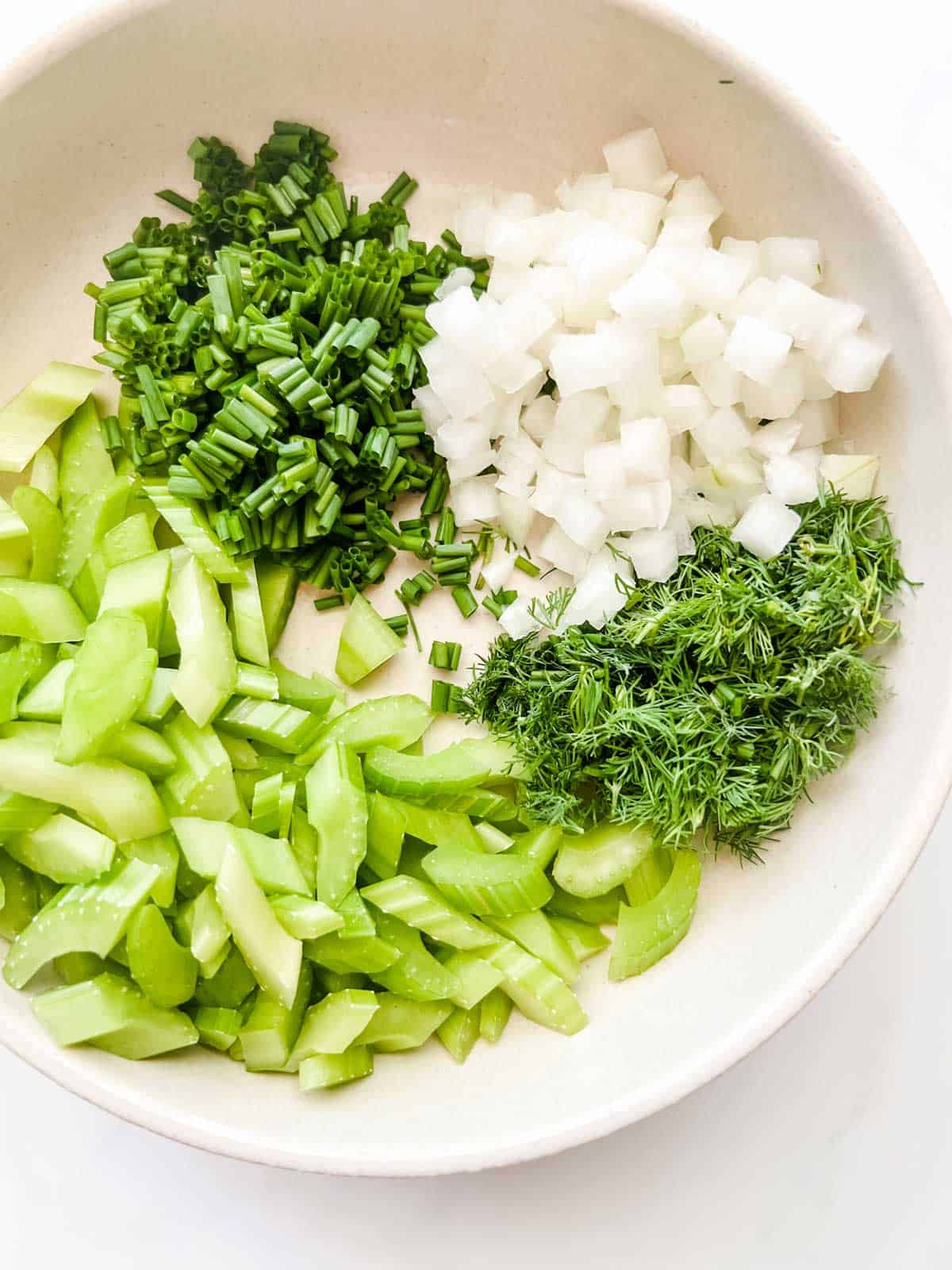 Photo of celery, onion, chives, and dill in a bowl.