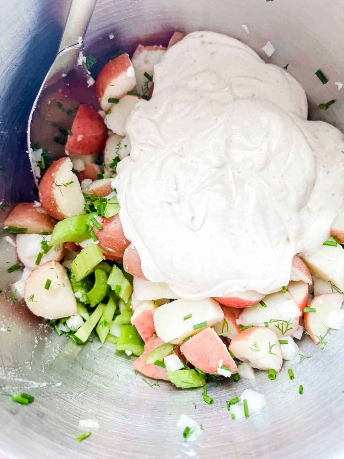 Photo of sour cream dressing that has been poured over potato salad in a bowl.