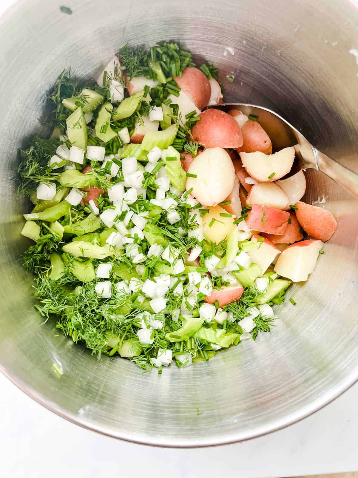 Photo of potatoes, celery, onion, dill, and chives in a large mixing bow.