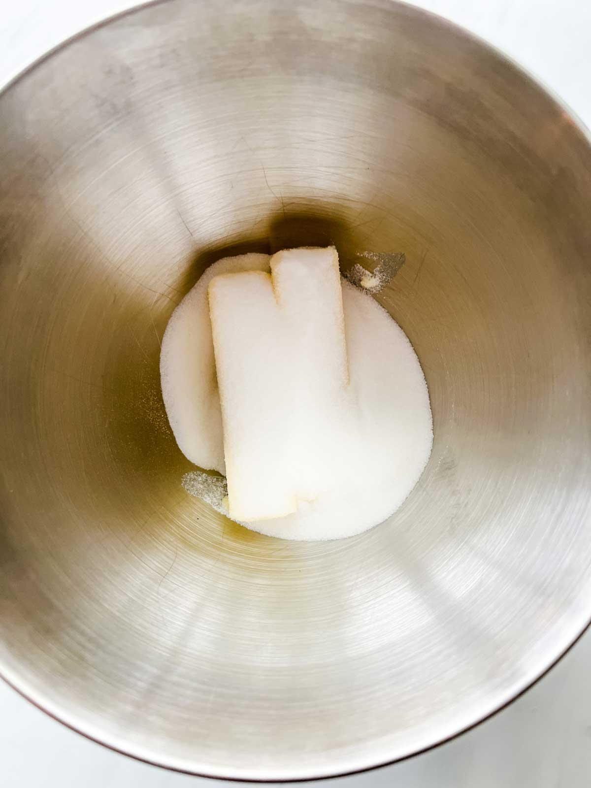 Photo of two sticks of butter and sugar in the bowl of a stand mixer.