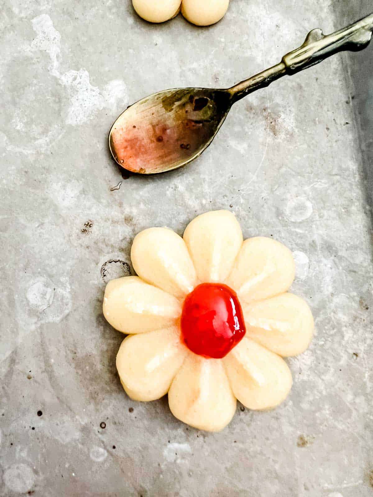 Photo of a spritz cookie on a baking sheet that has just had jam added to the center.