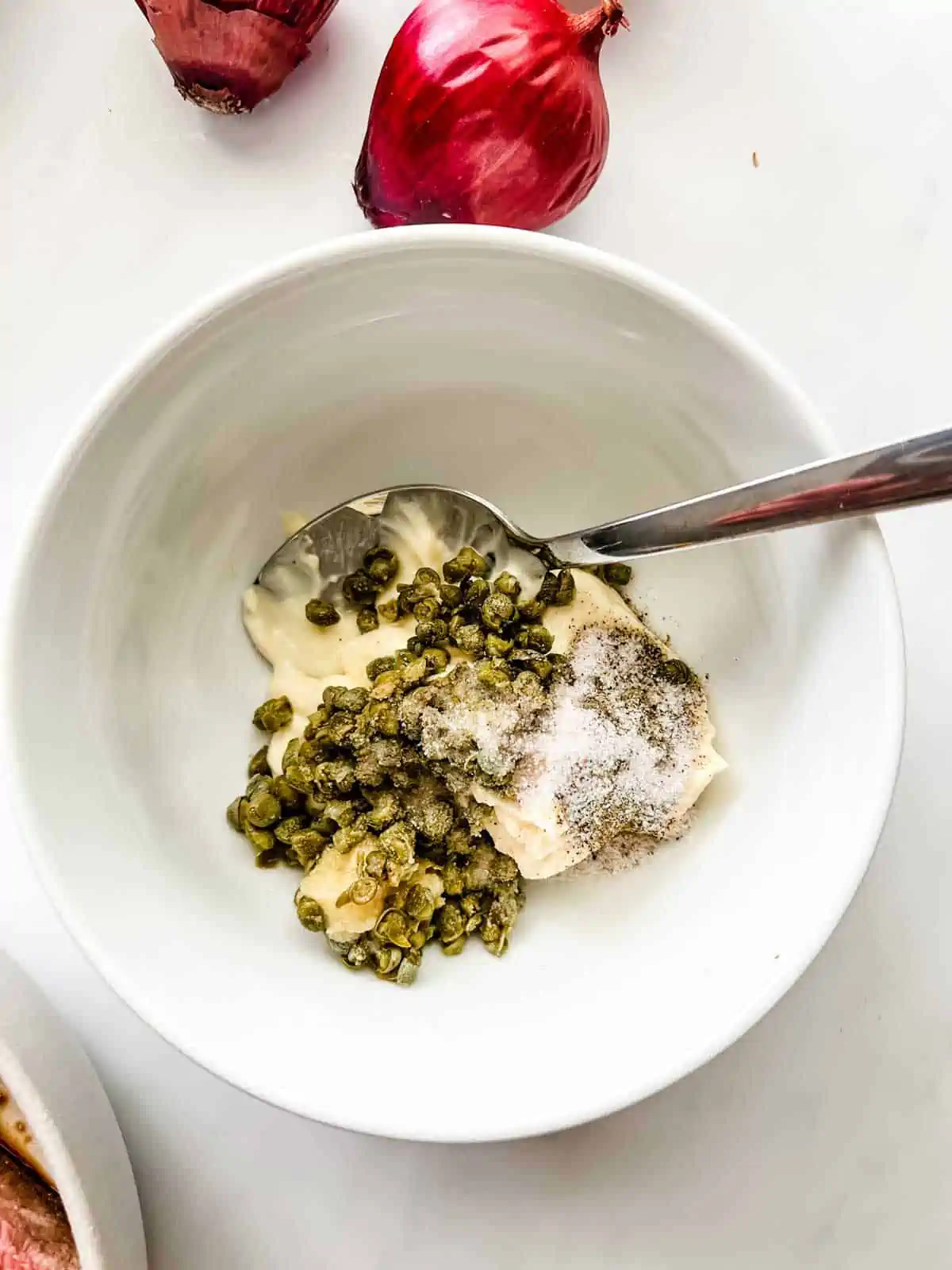 Mayonaise, capers, and seasonings in a small white bowl.