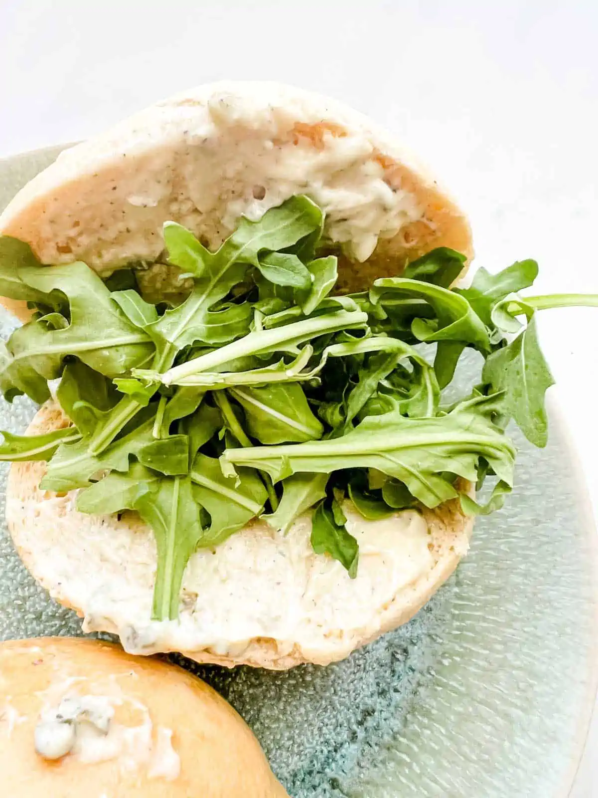 Photo of sandwich buns with an aioli spread and arugula.