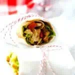 Square photo of a guacamole wrap in parchment tied with red and white string.