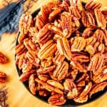 Close up square photo of a small bowl of air fryer pecans.