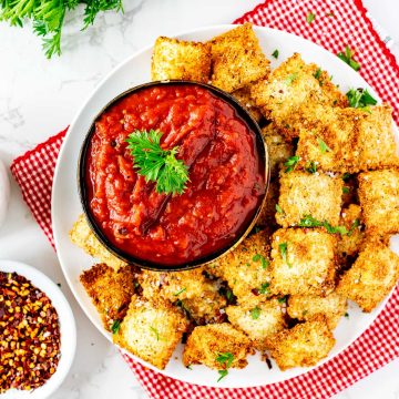 Square overhead photo of a white plate of crispy breaded air fryer ravioli with a small dish of marinara sauce.