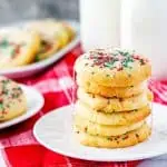 Square photo of a plate of stacked air fryer sugar cookies with two other plates of cookies and milk bottles around it.