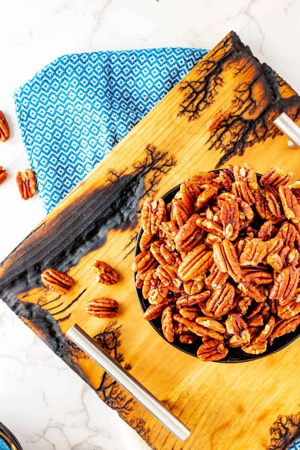 Overhead photo of a rustic board with a bowl of candied pecans made in the air fryer.
