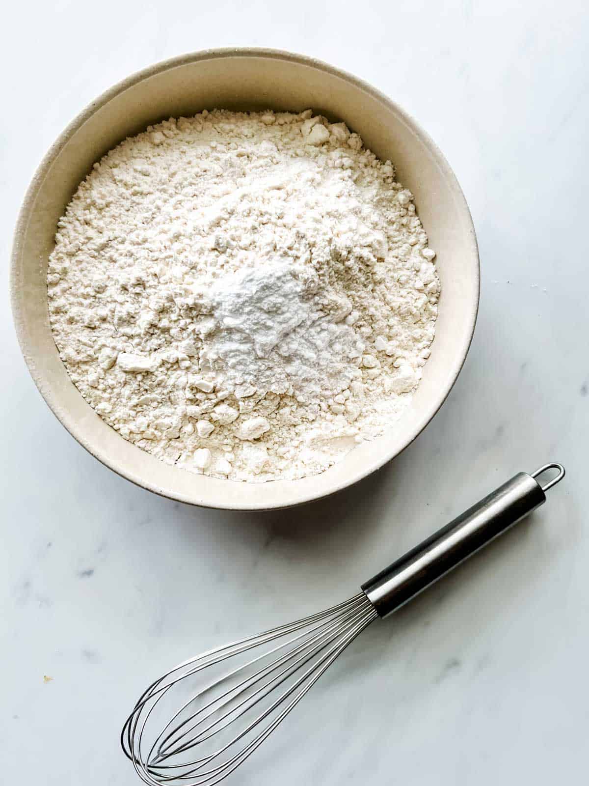 Photo of dry ingredients for cookies in a bowl with a whisk next to it.