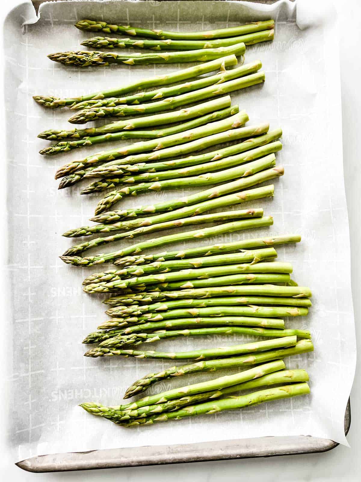 Parchment lined sheet pan with asparagus on it.