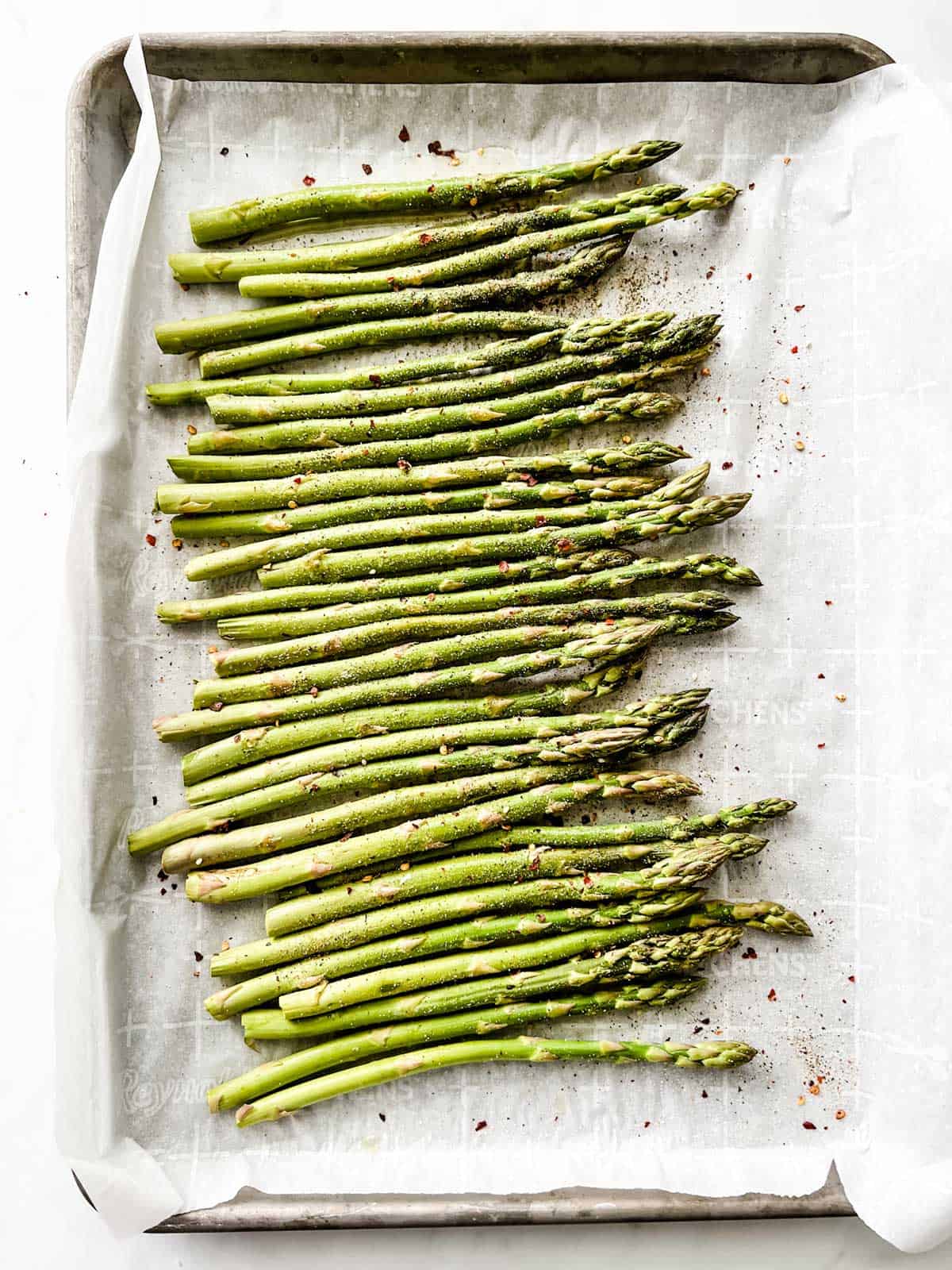 Parchment lined baking sheet with seasoned asparagus.