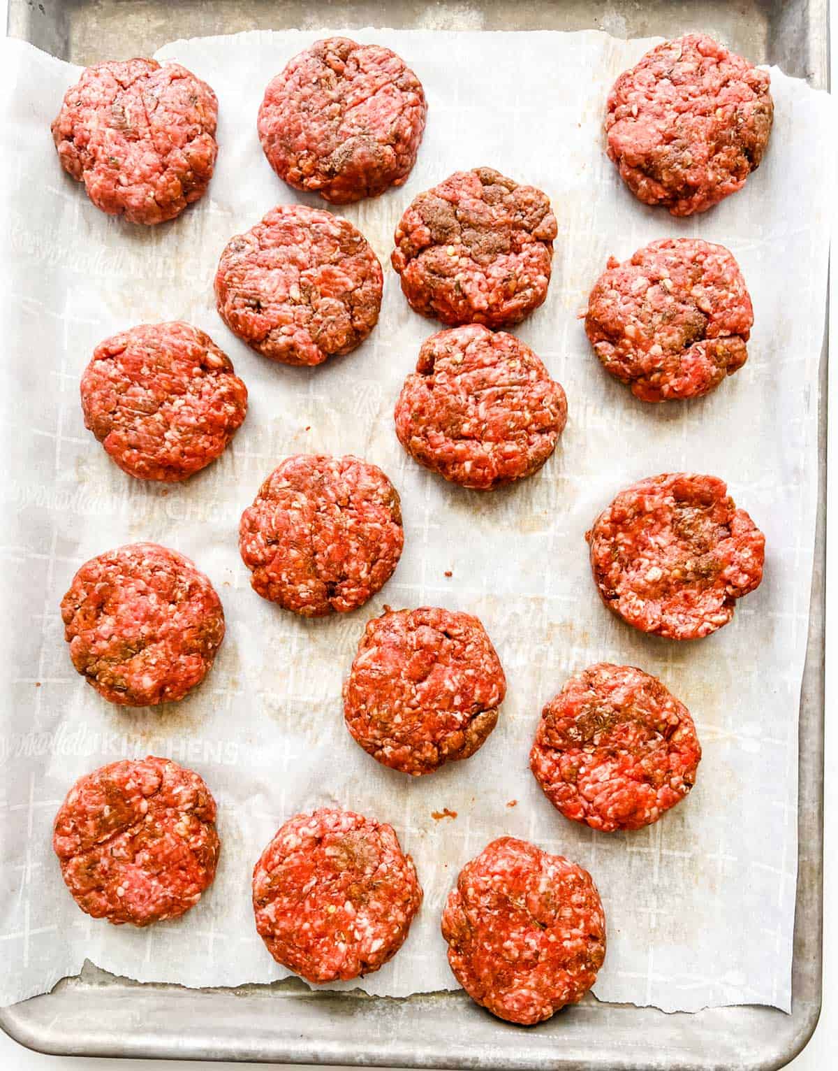 A parchment lined baking sheet with uncooked sausage patties.