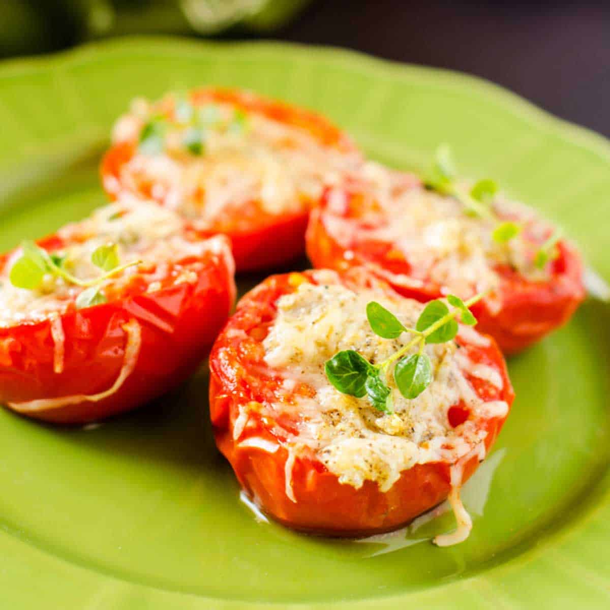 Square close up photo of broiled tomatoes with cheese on a green plate garnished with thyme.