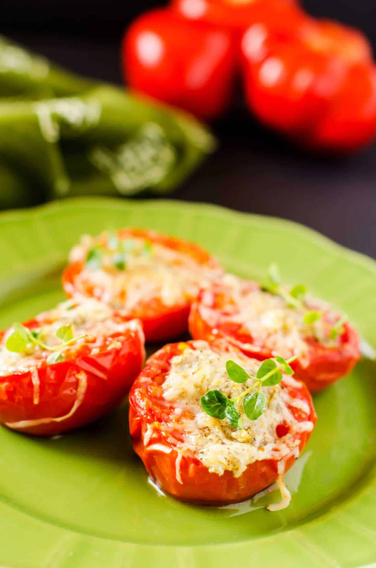 Close up photo of broiled tomatoes with cheese on a green plate garnished with thyme.