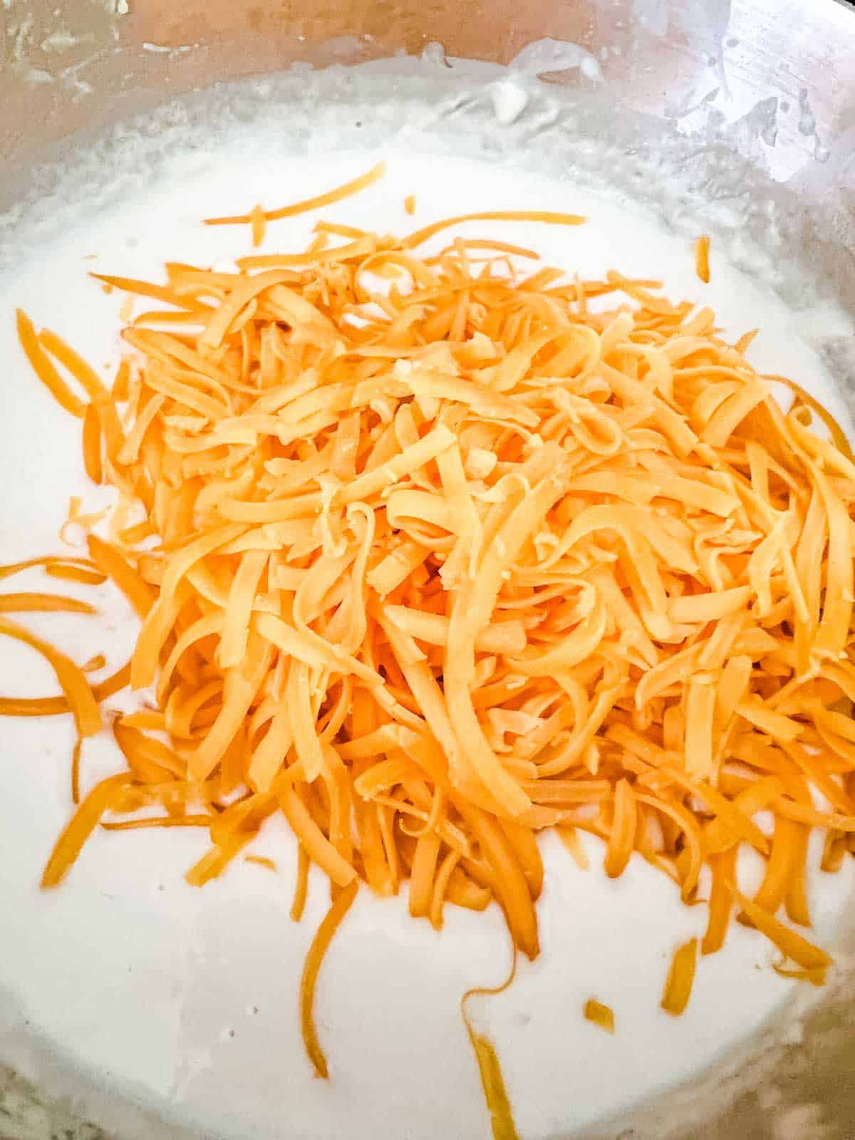 Photo of shredded cheese that has just been added to a cream sauce.