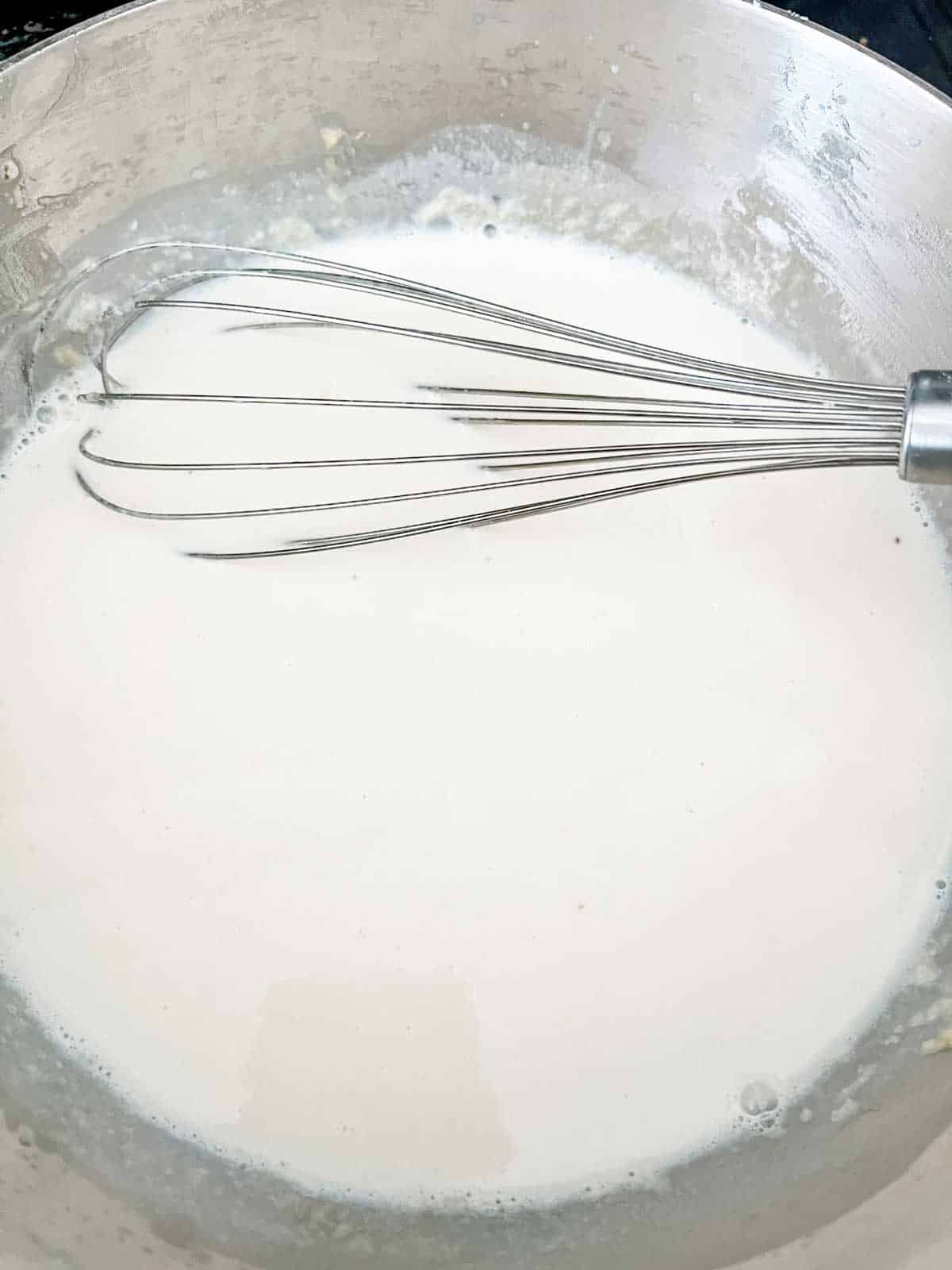 Photo of milk that has been added to butter and flour in a skillet.