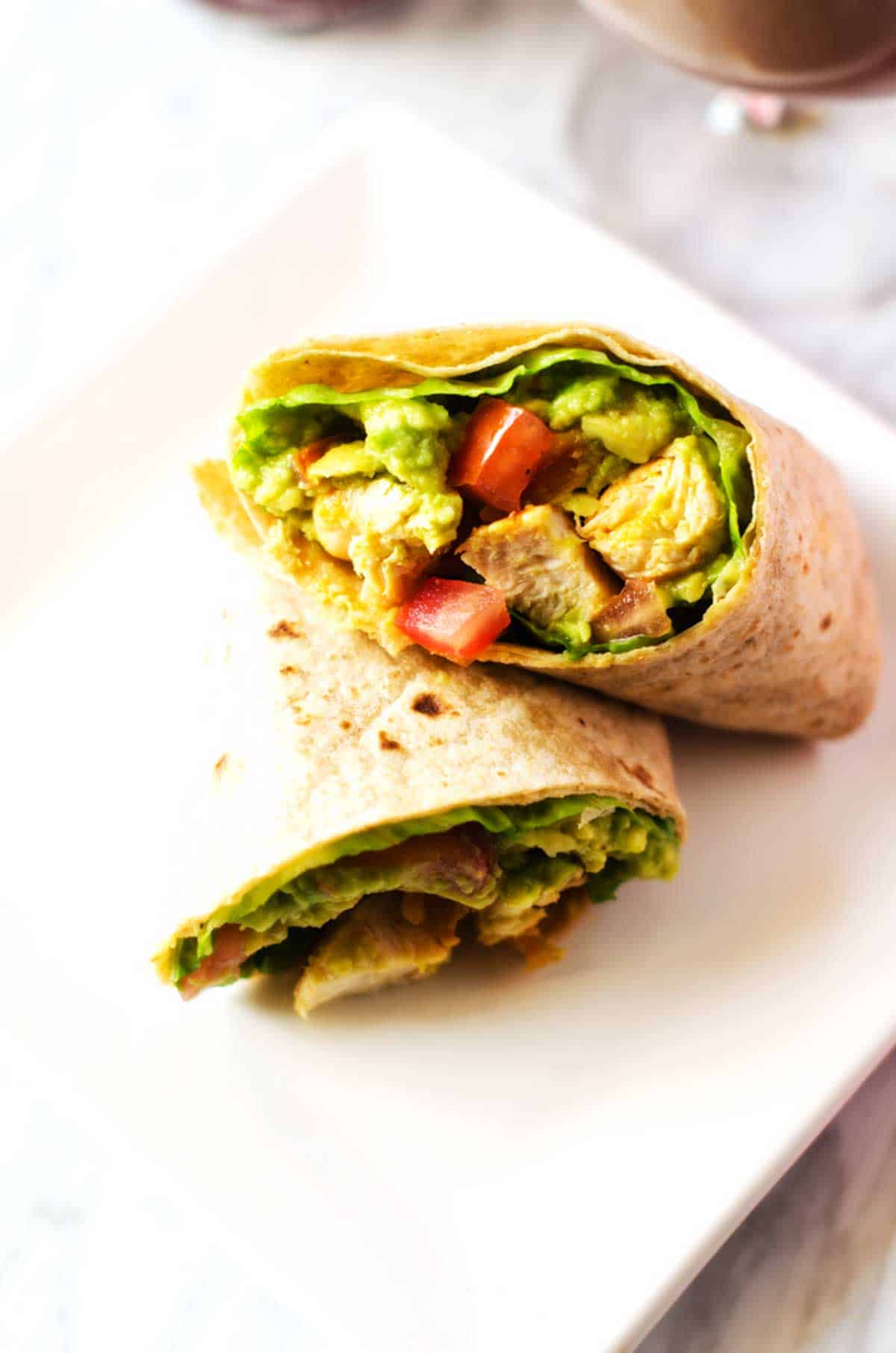 Close up photo of a white plate with an avocado guacamole and chicken wrap.