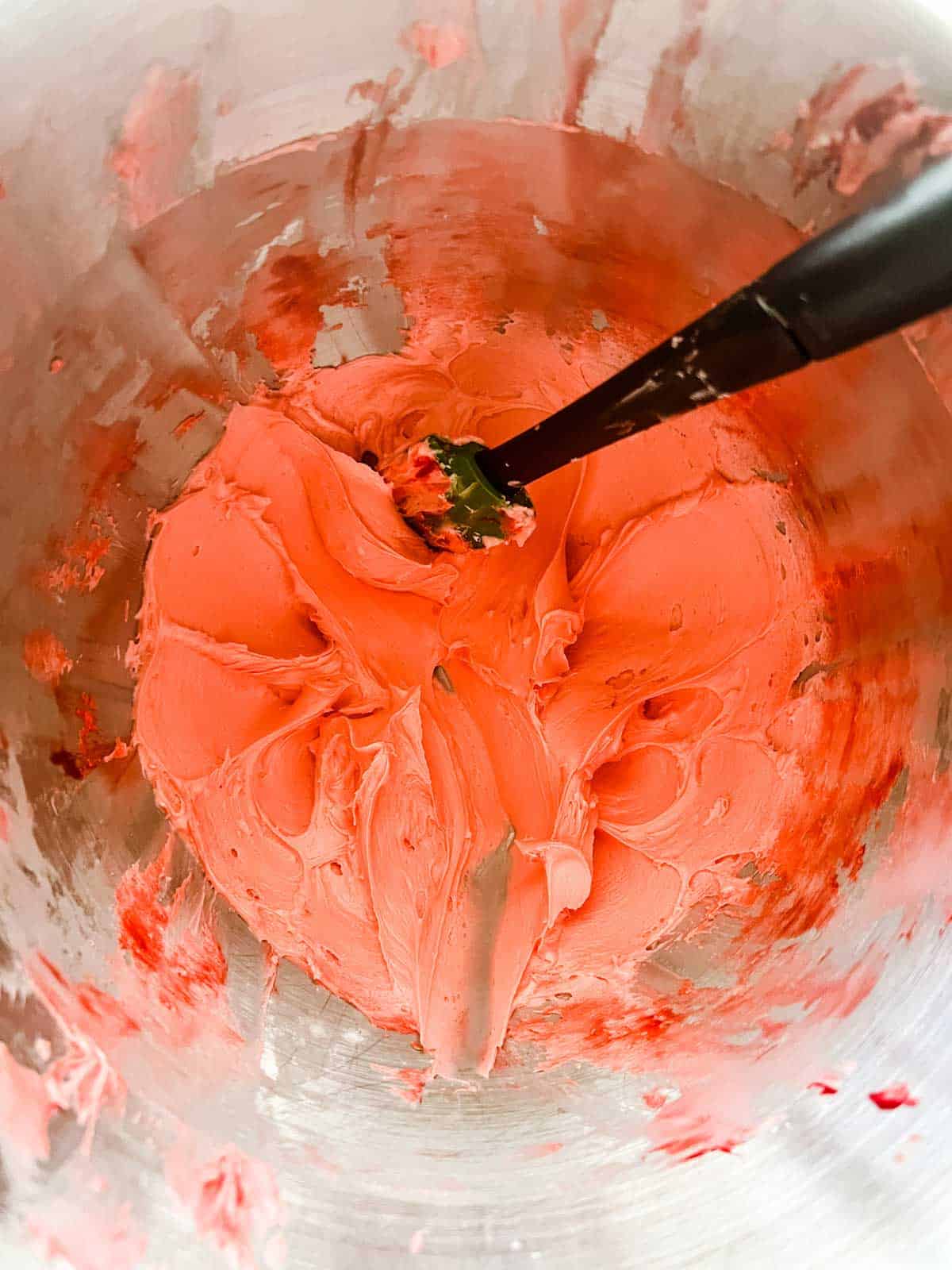 Photo of red peppermint icing in the bowl of a stand mixer with a rubber spatula.