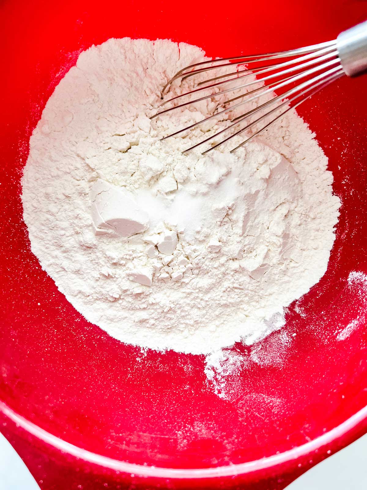 Dry cookie ingredients being whisked together in a red bowl.