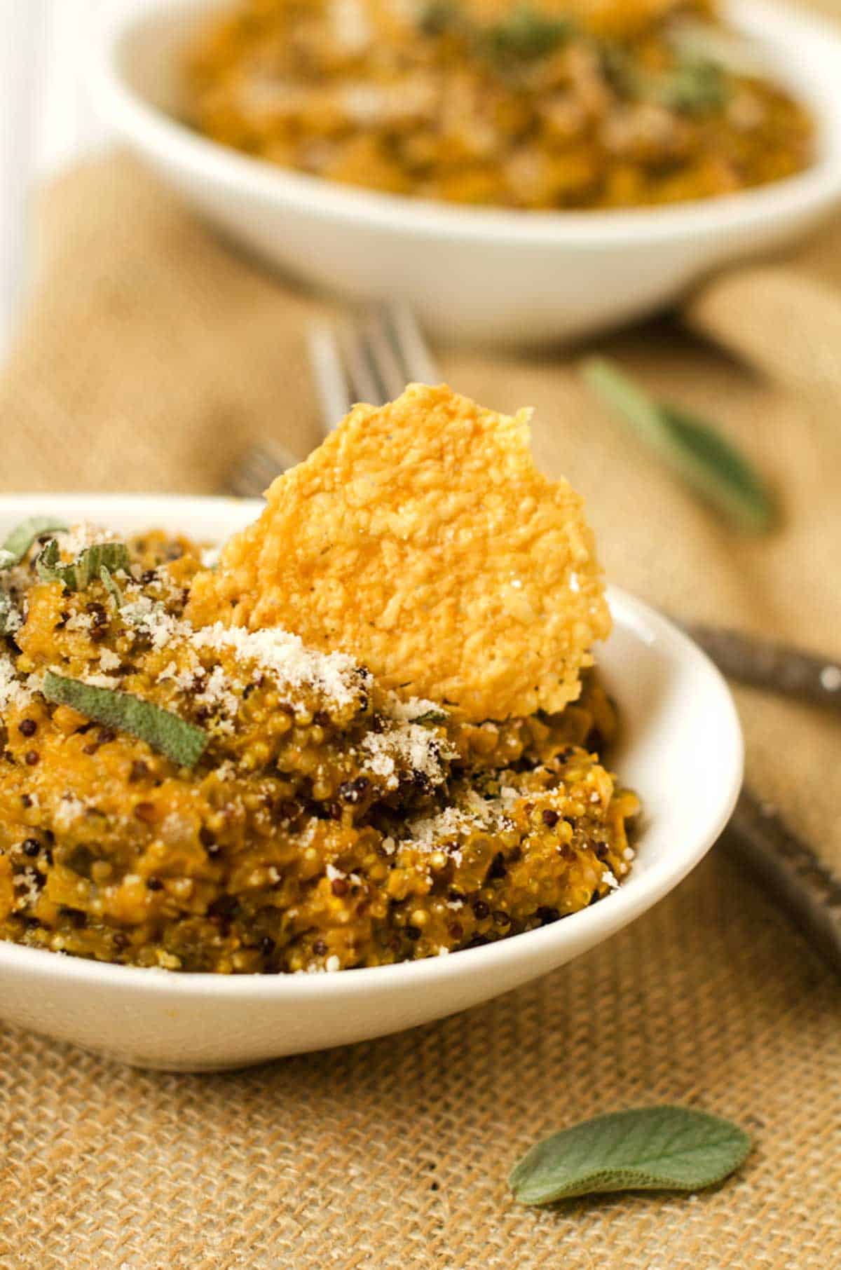 Close up photo of a bowl of quinoa risotto garnished with sage, parmesan, and a parmesan crisp.