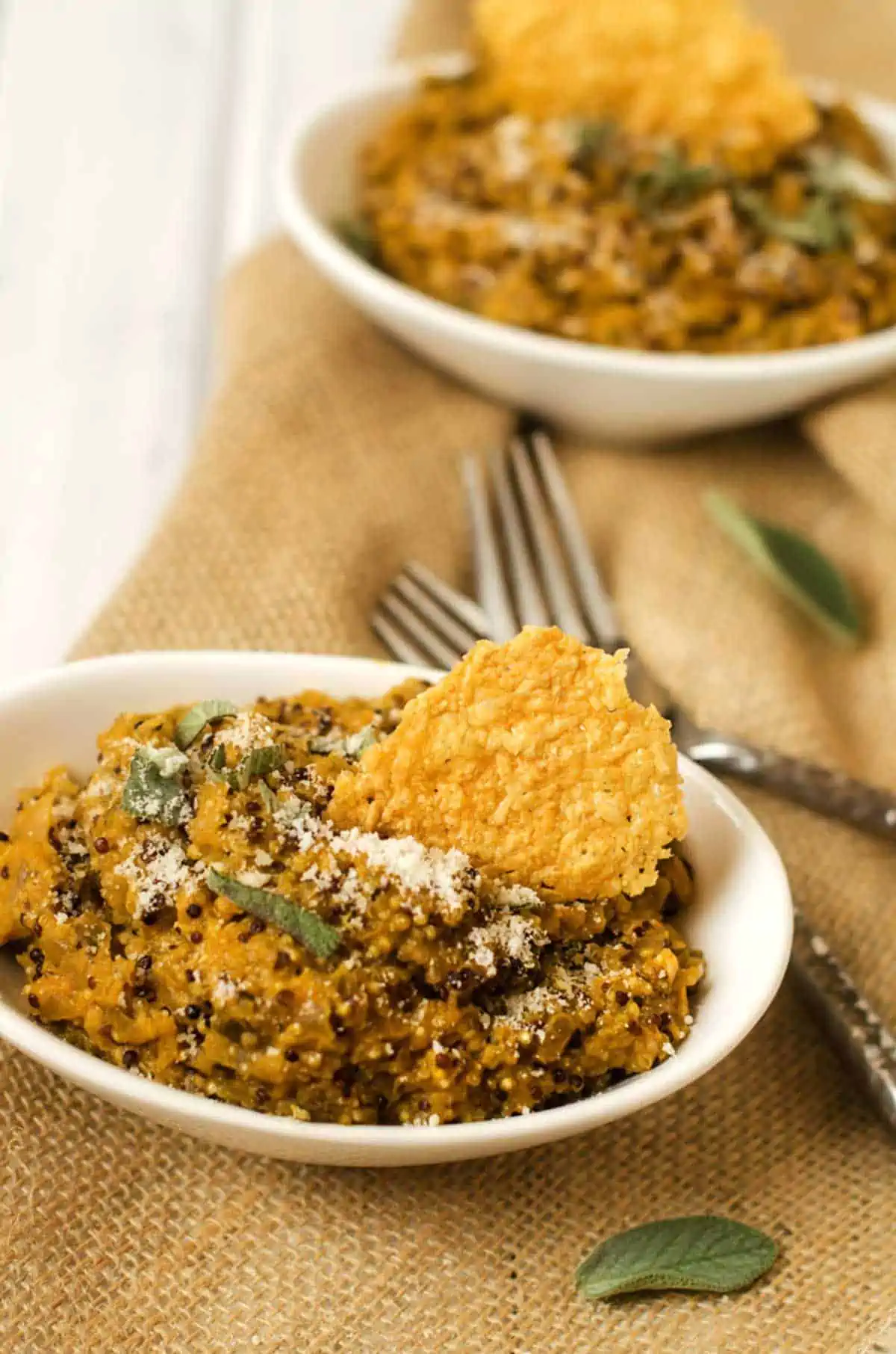 Side photo of two bowls of pumpkin quinoa risotto garnished with parmesan crisps.