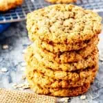 Square photo of a stack of oatmeal cookies sitting in front of more cookies on a cooling rack.