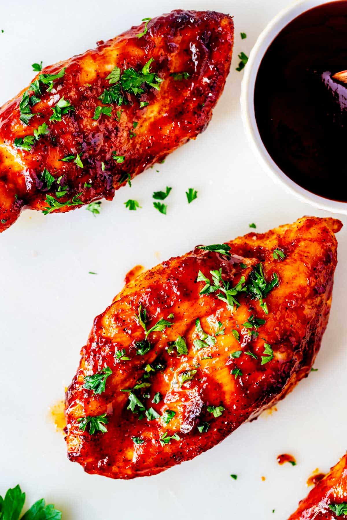 Photo of BBQ Chicken Breast on a white background with a small bowl of BBQ sauce sitting next to it.