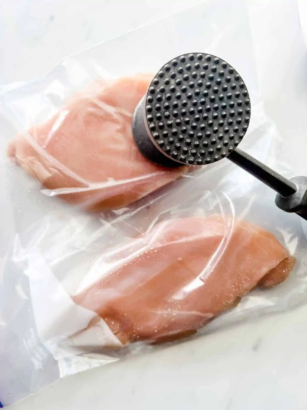 Chicken in a plastic bag being pounded with a meat mallet.
