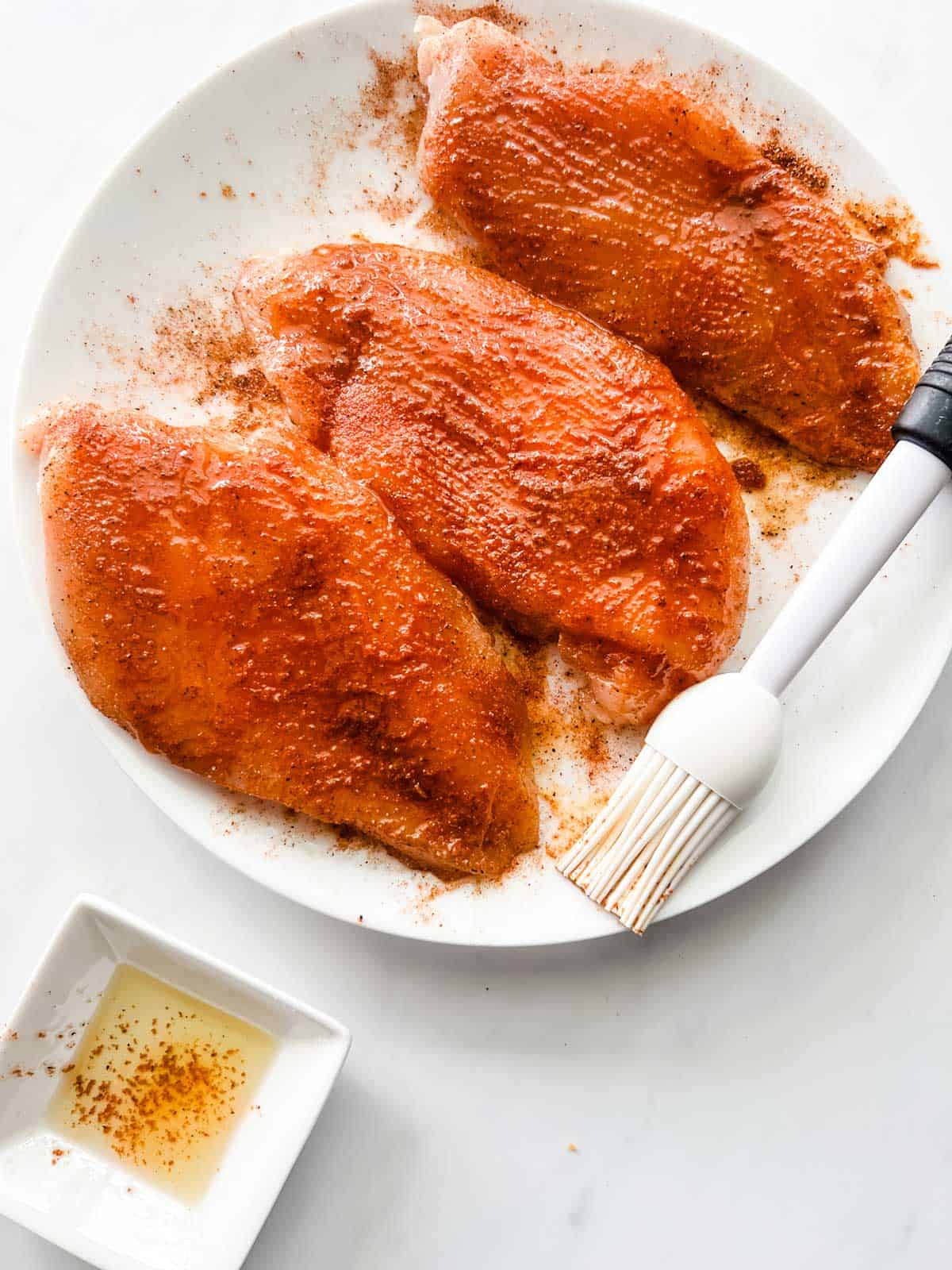Seasoned chicken breast being brushed with oil.