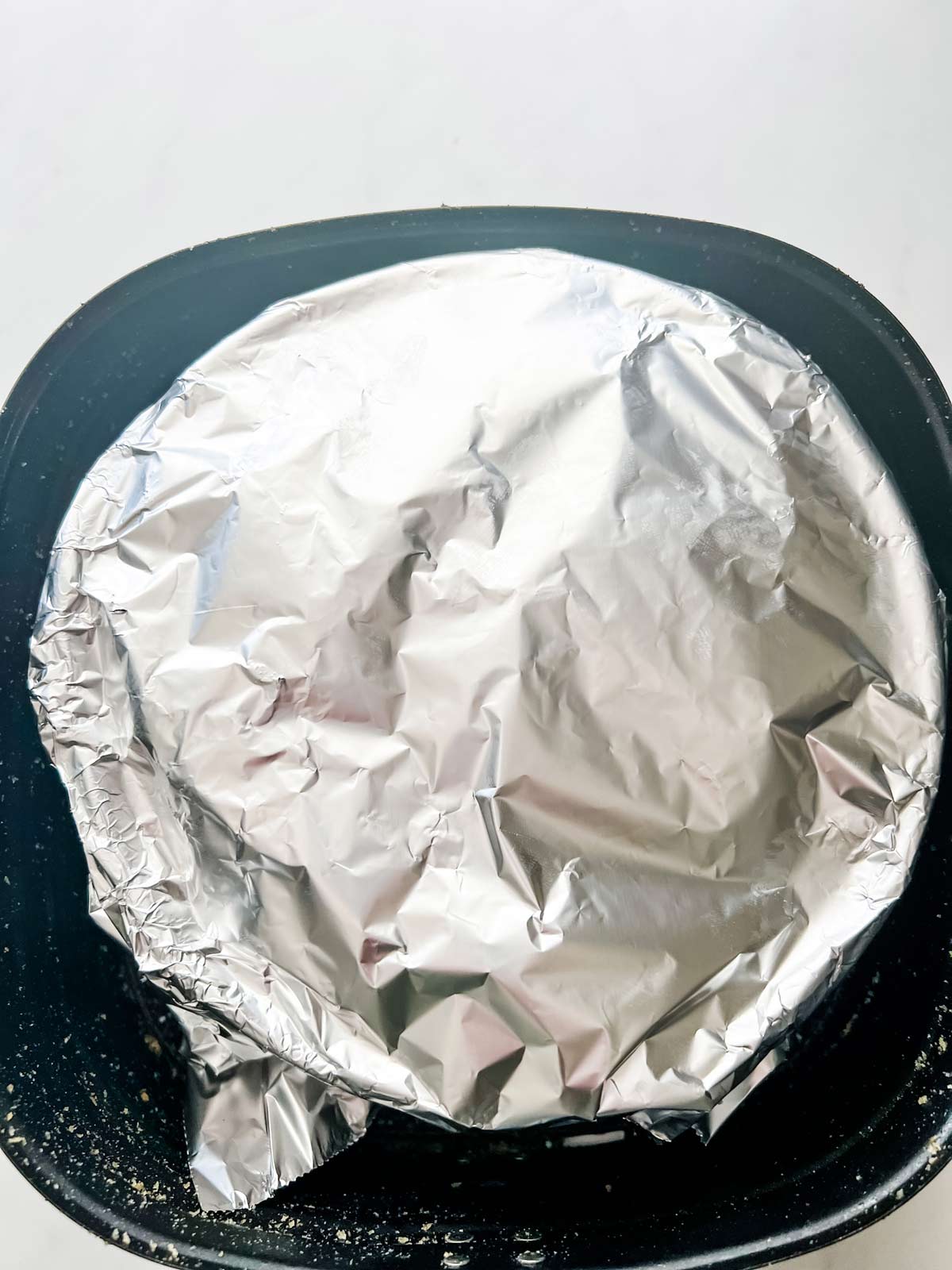 A round casserole dish with foil over it in an air fryer.
