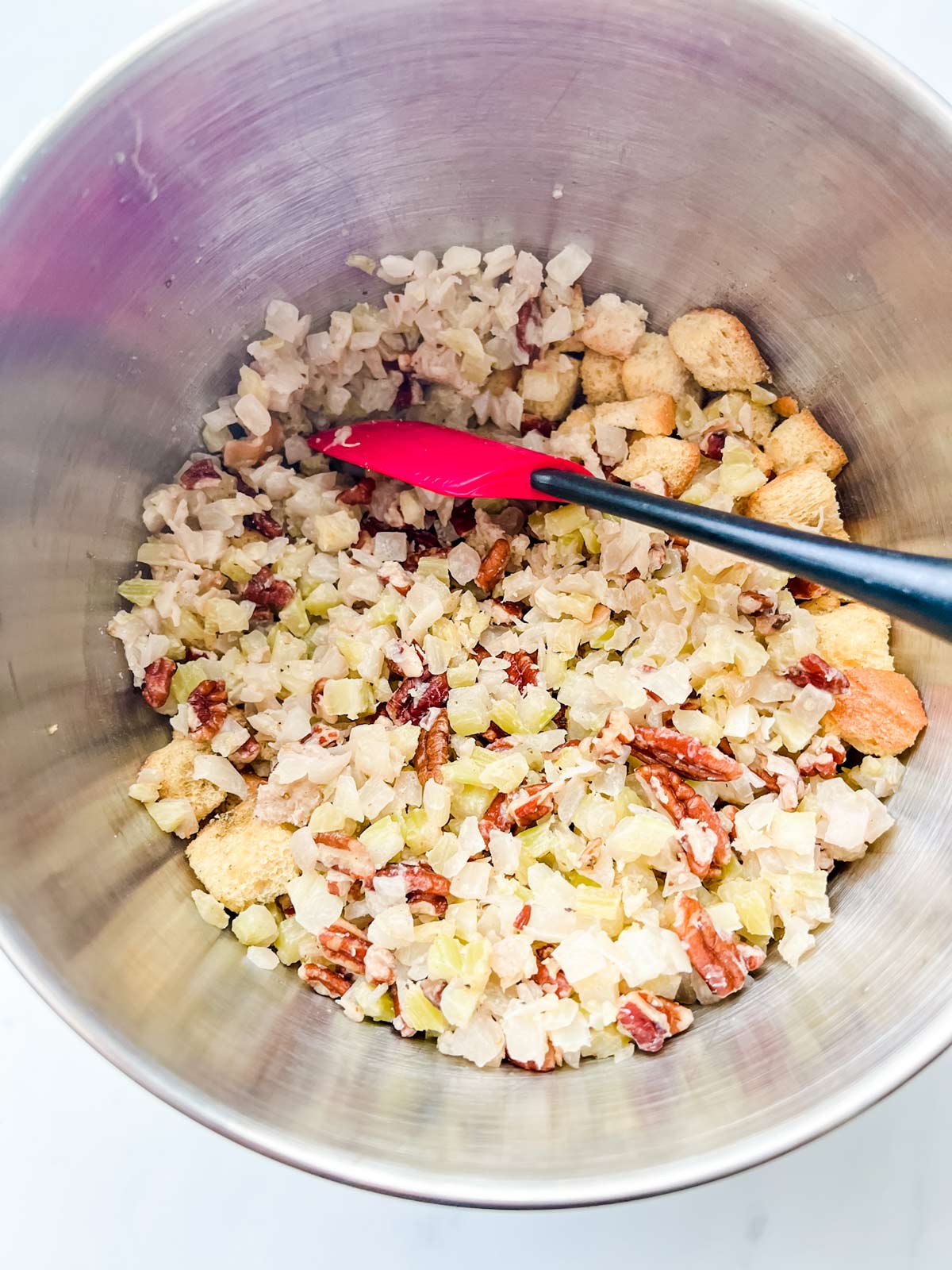 Bread cubes, onion, celery, pecans, and seasonings being tossed in a bowl.