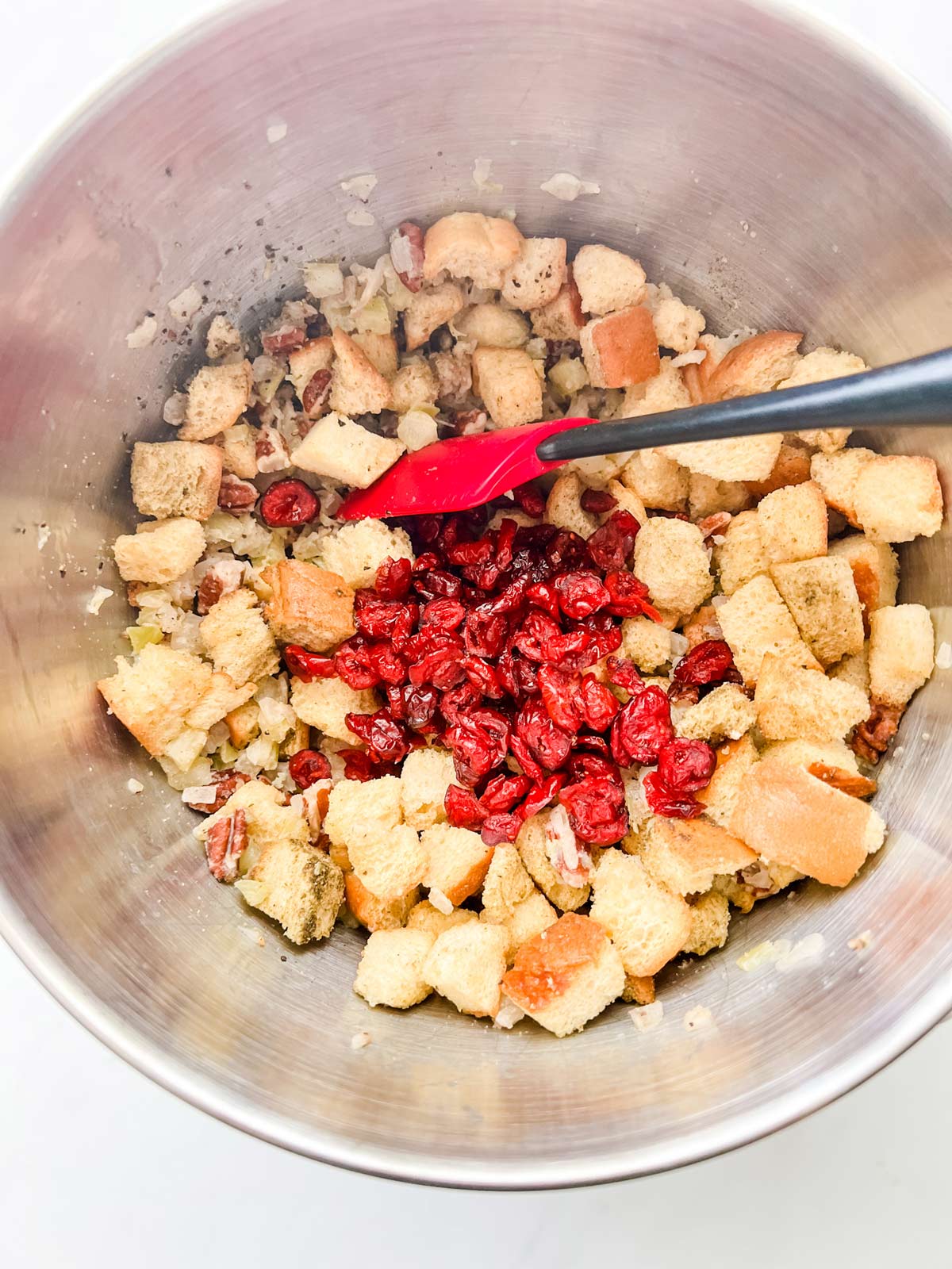 cranberries being tossed in a bowl with the remaining stuffing ingredients.