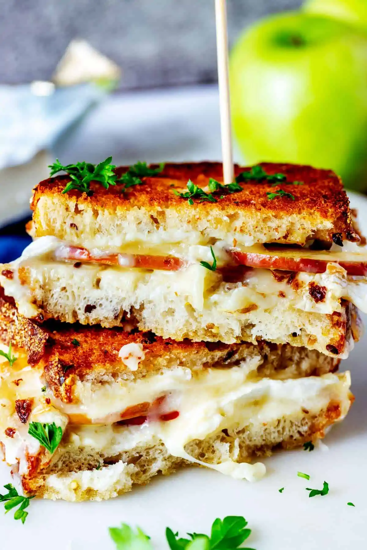 Photo of a stacked apple brie sandwich on a marble board garnished with parsley.