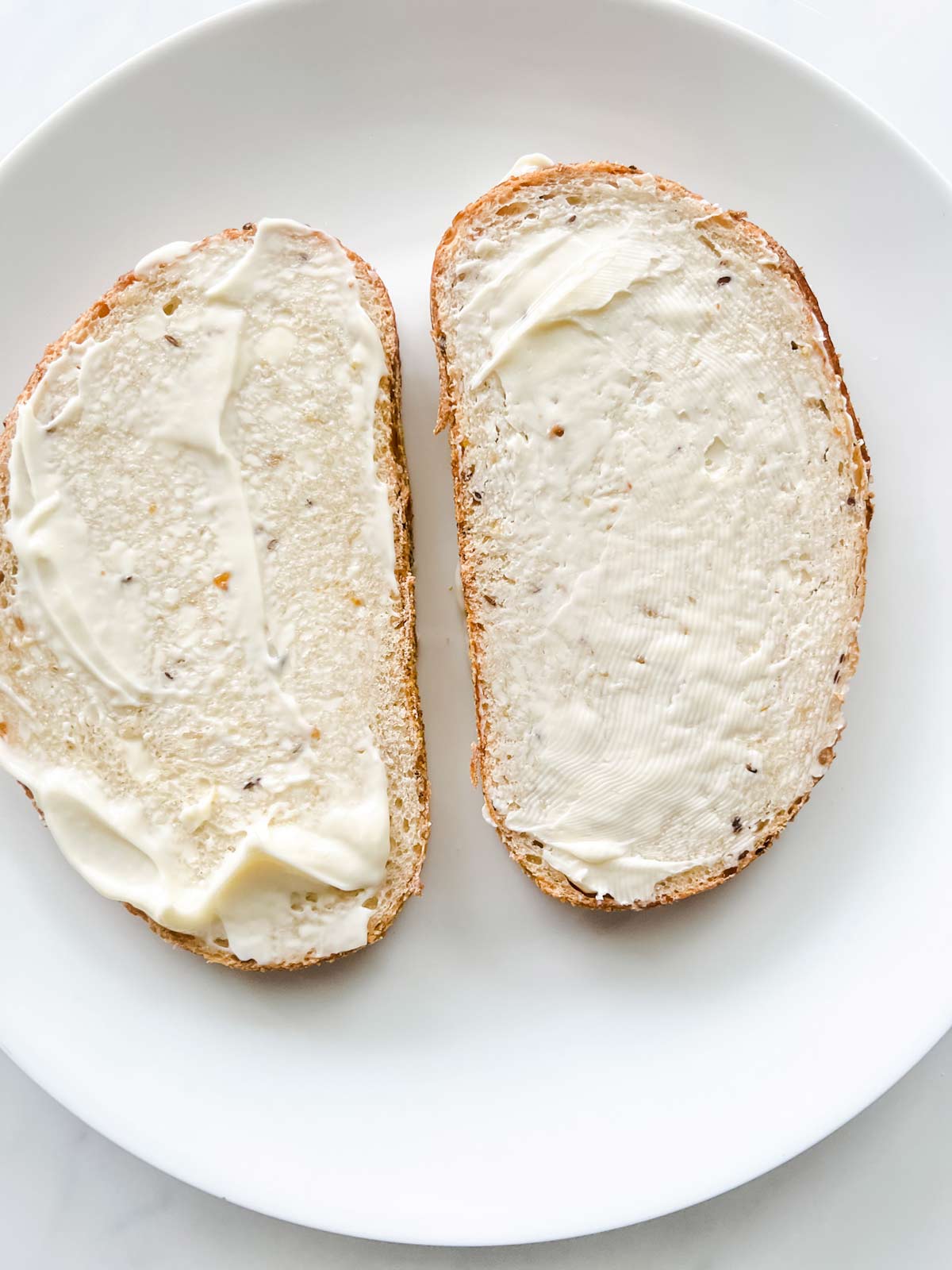 Photo of two slices of bread with mayonnaise on them.