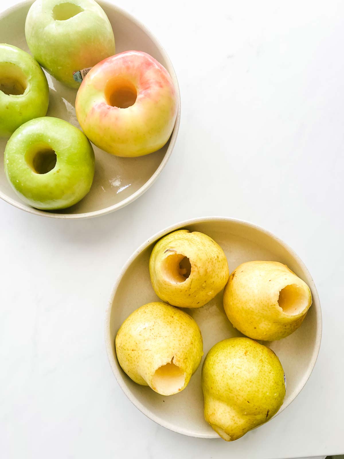 Overhead photo of a bowl of cored apples and a bowl of cored pears.