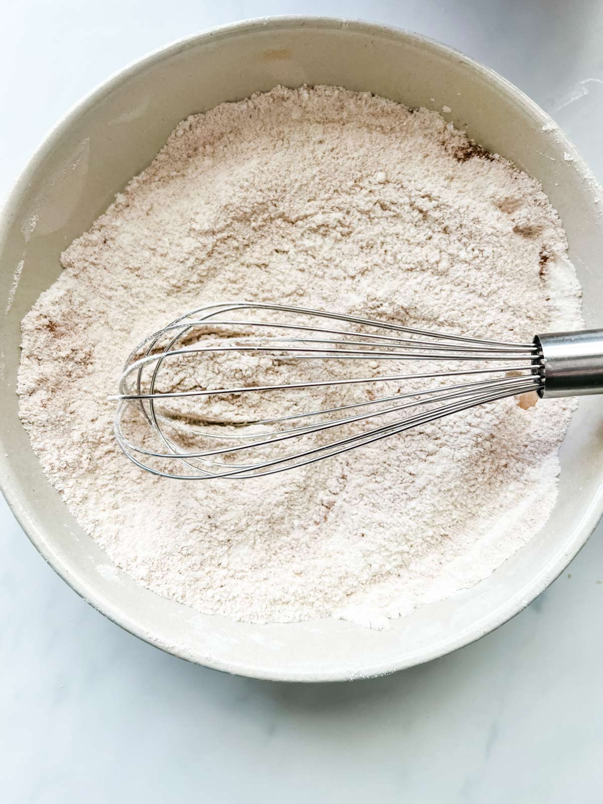 Overhead photo of flour, sugar, and cinnamon being whisked together in a bowl.
