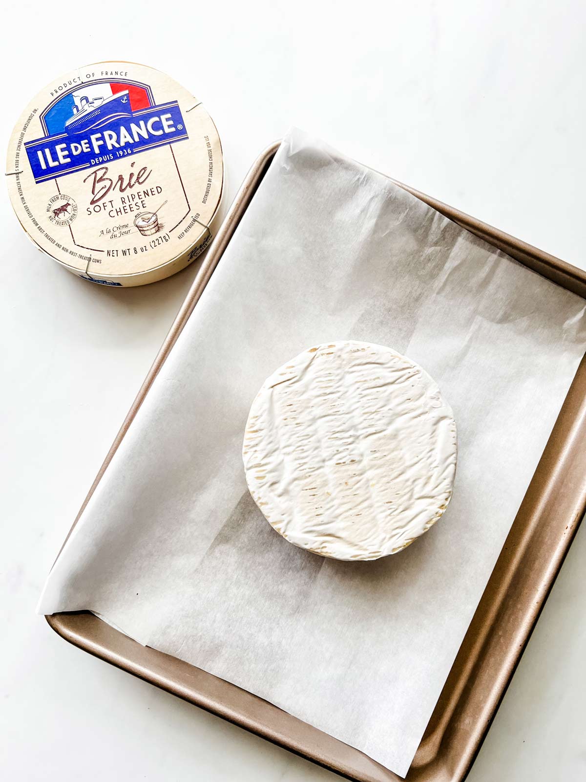 Photo of brie on a small parchment lined baking sheet.