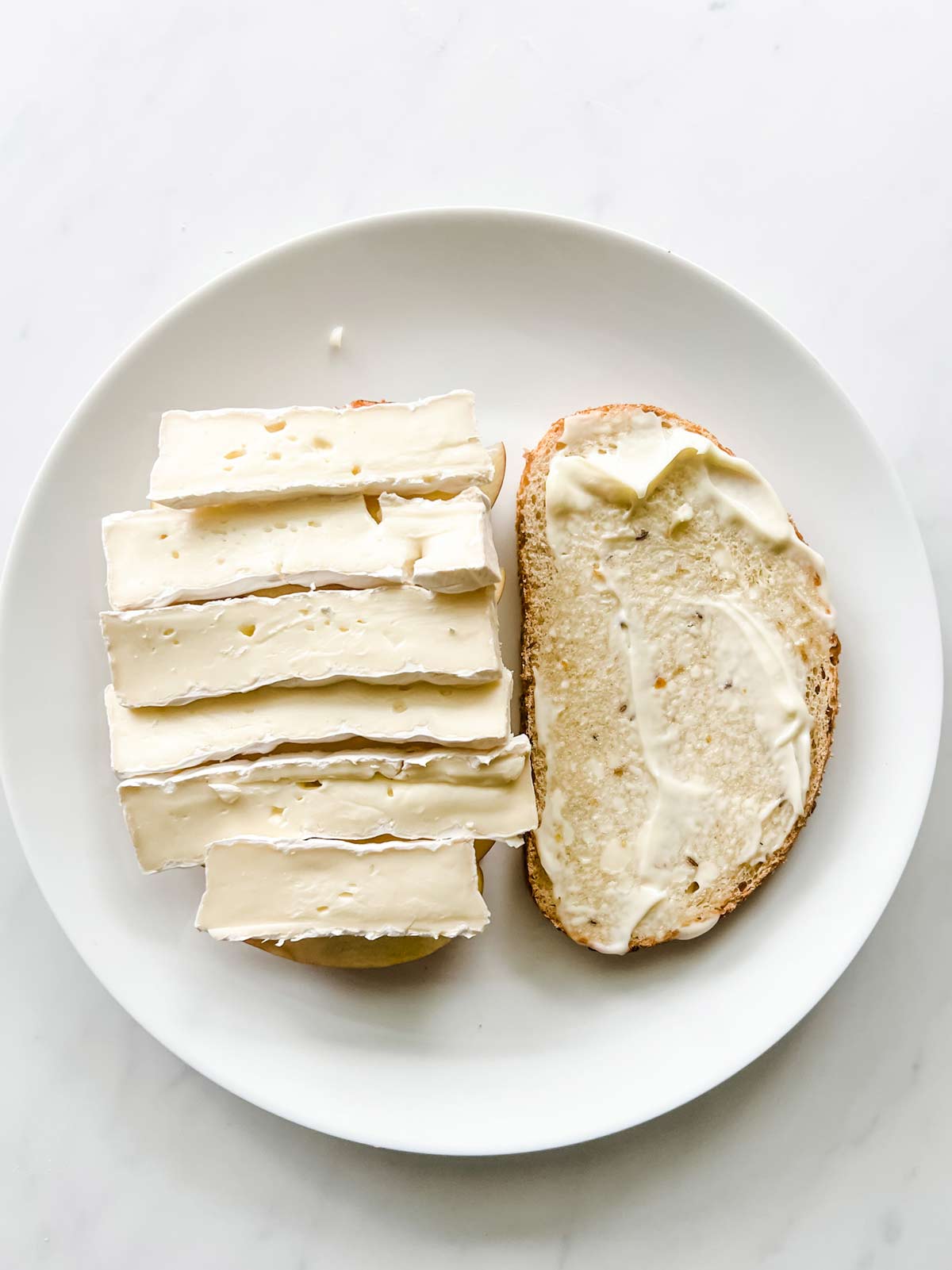 Photo of a slice of bread with brie and another with mayonnaise.