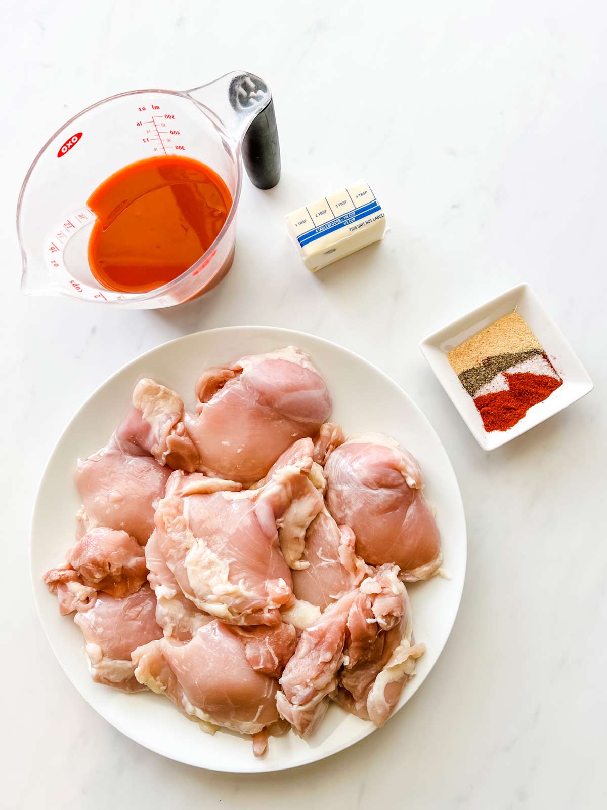 Oerhead photo of chicken thighs, buffalo sauce, butter, and seasonings in prep bowls.