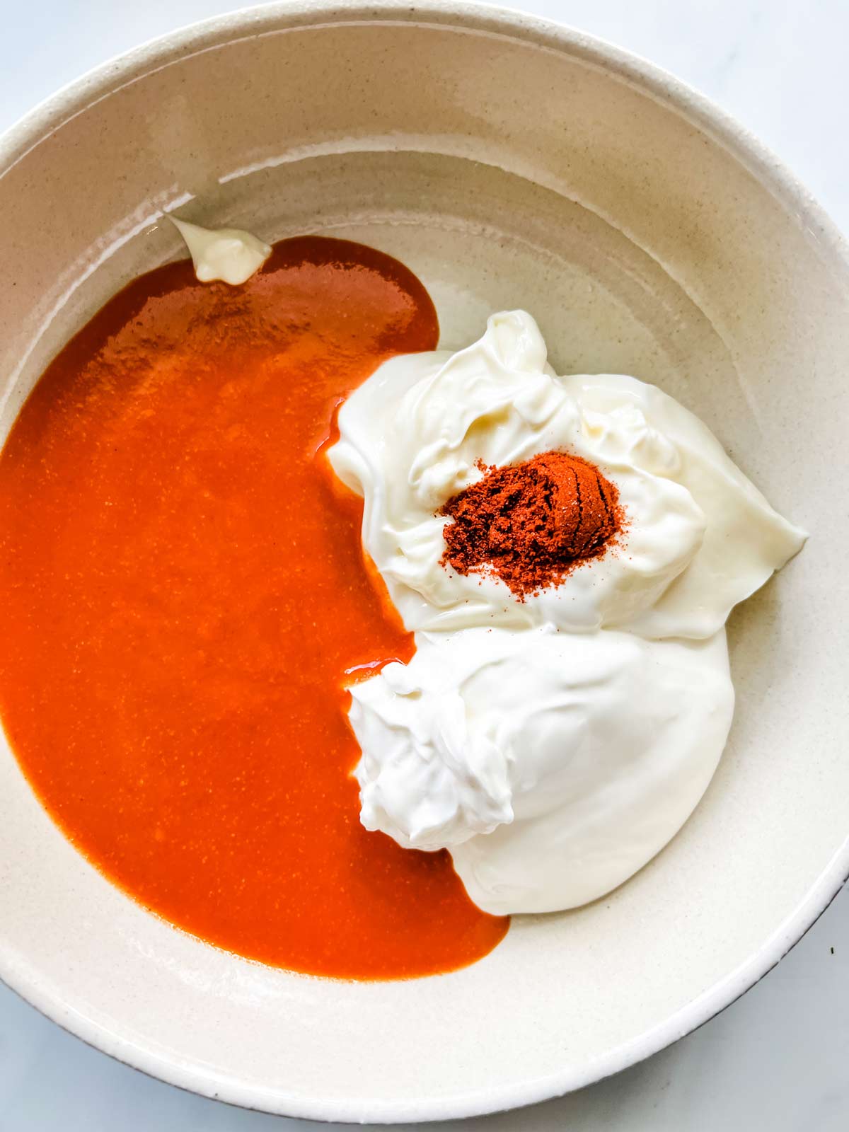 Sour cream, mayonnaise, hot sauce, and seasonings in a bowl.