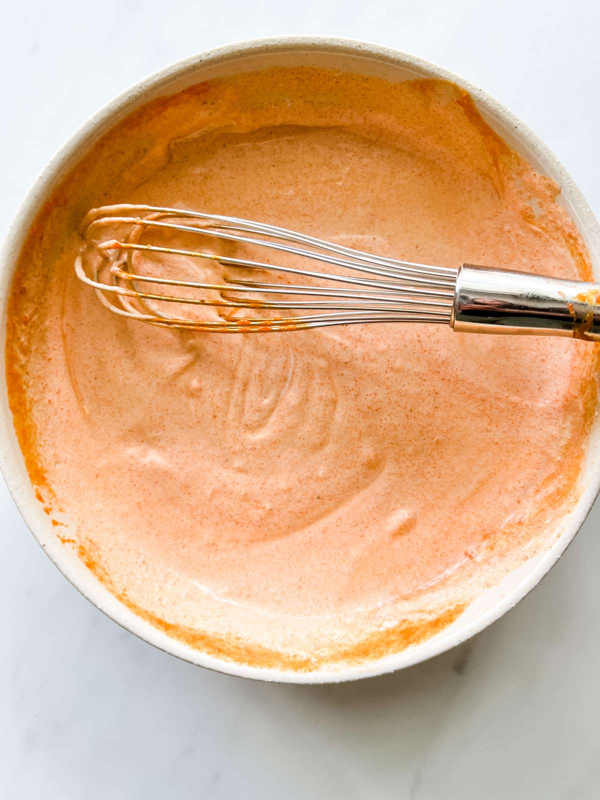 Creamy buffalo sauce with a whisk in a bowl.