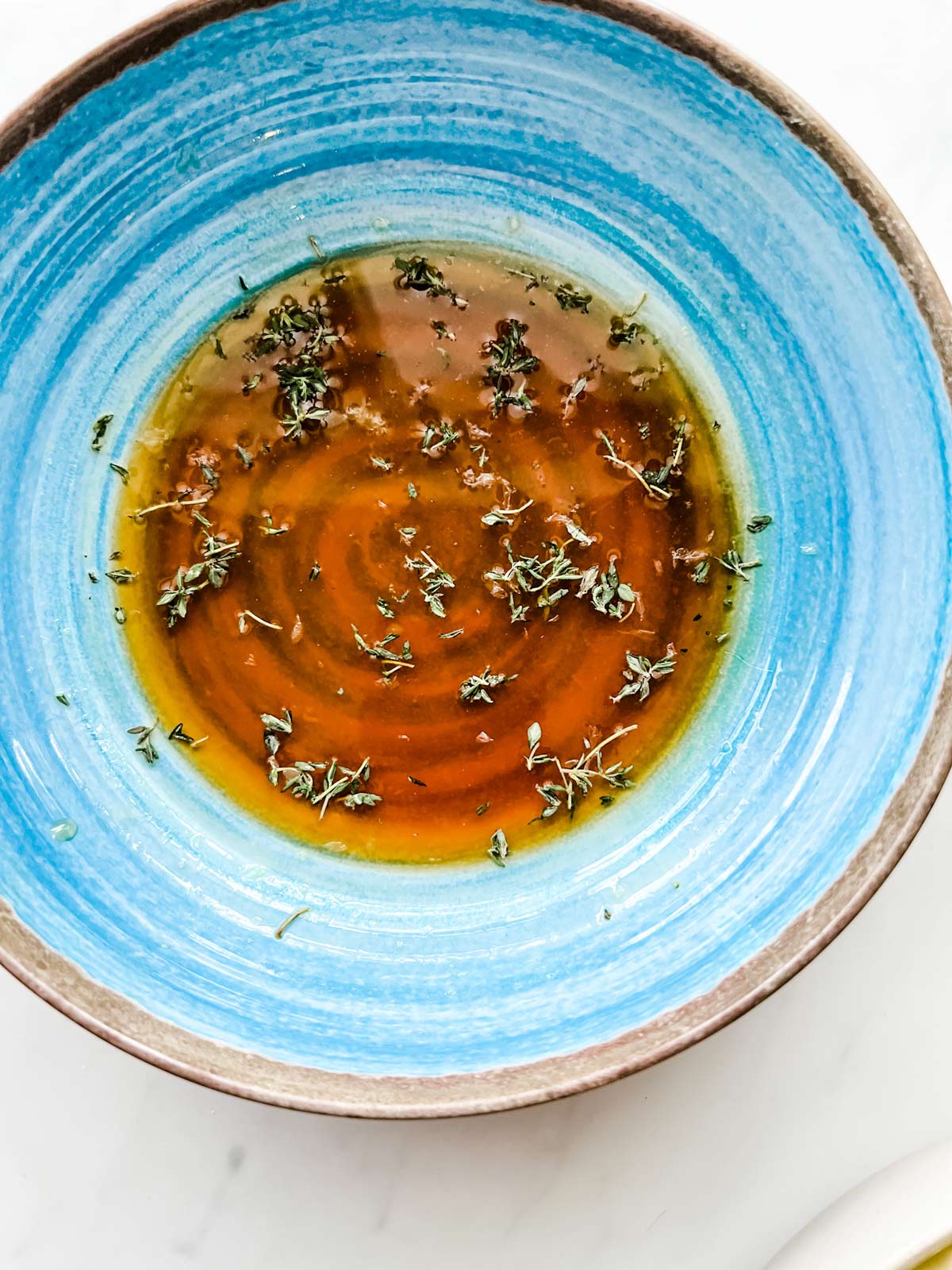 Photo of a small blue bowl with thyme, maple syrup, soy sauce, and lemon juice.