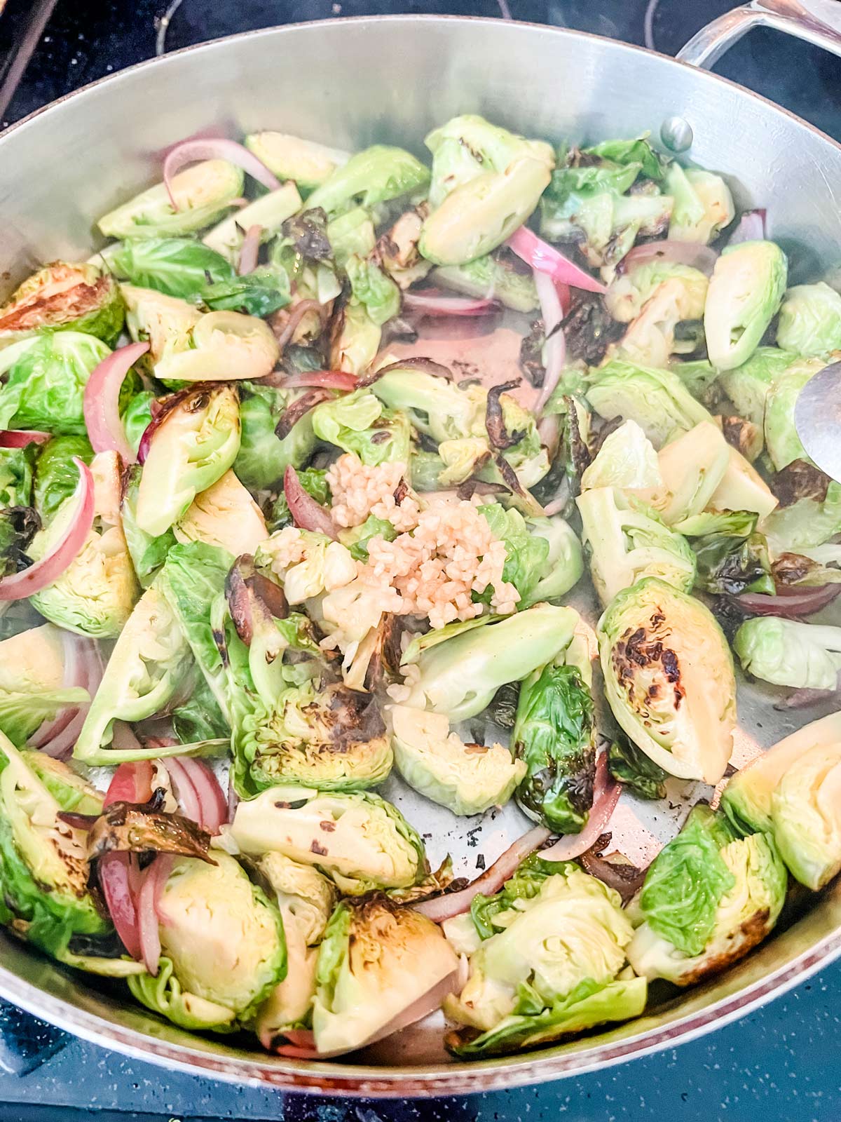 Brussels sprouts and onion in a large skillet with garlic over it.