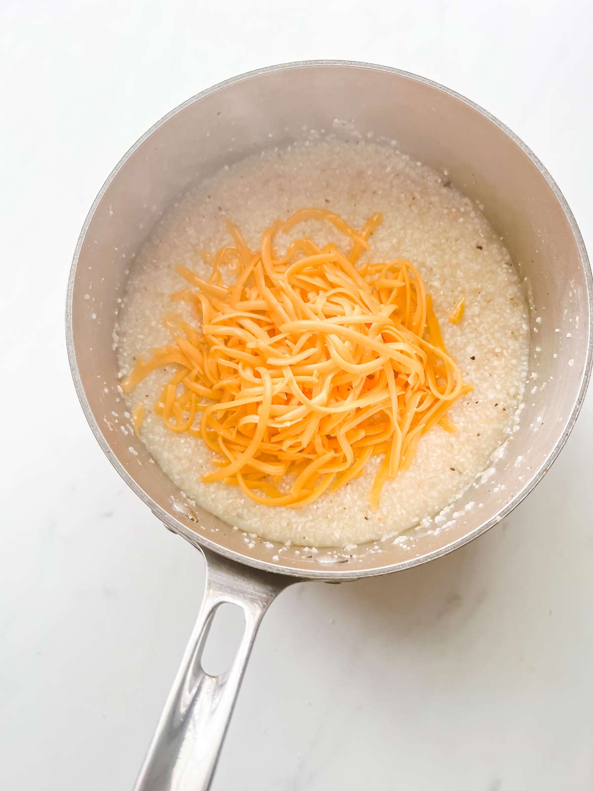 Shredded cheese on top of grits in a saucepan.