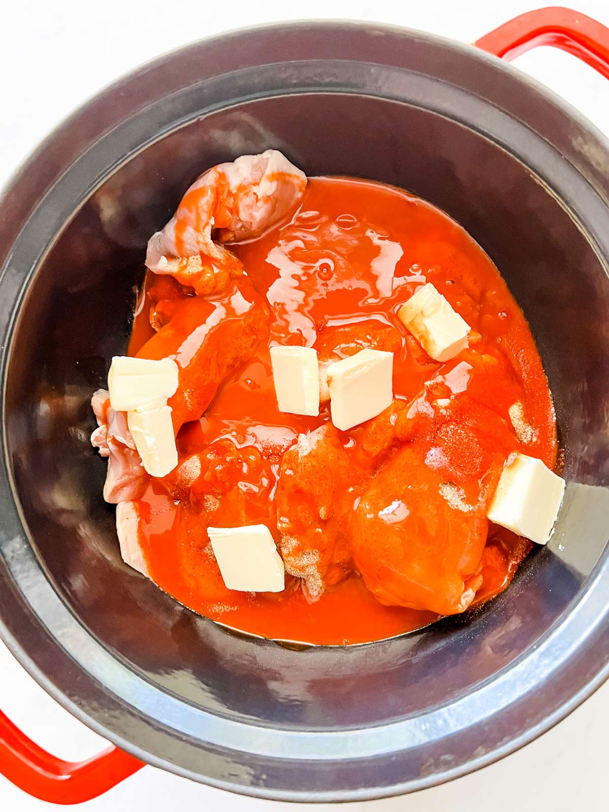Photo of chicken thighs, seasonings, buffalo sauce, and butter in a slow cooker.