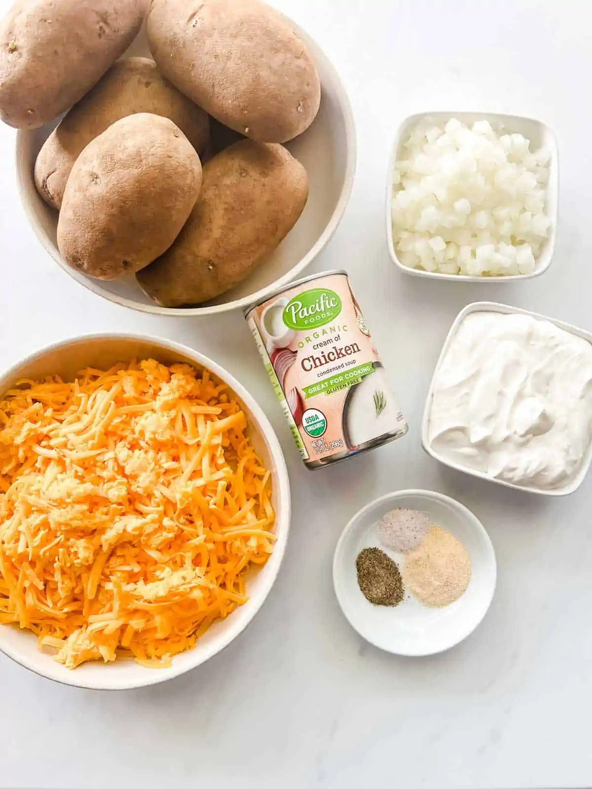 Overhead photo of a bowl of potatoes, can of soup, and prep bowls with shredded cheese, seasonings, diced onion, and sour cream.