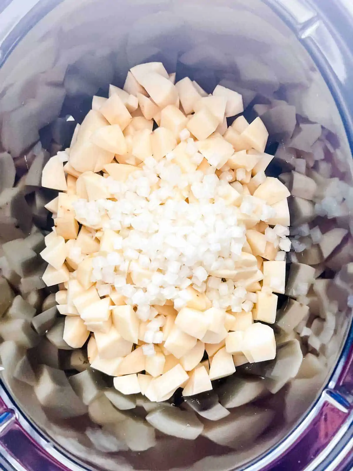 Photo of diced potatoes and onion in a slow cooker.